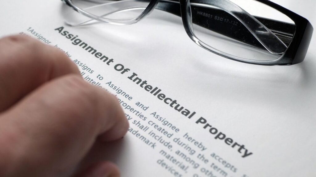 Close-up of an intellectual property assignment form on a lawyer’s desk. Fingers and a pair of eyeglasses are visible.